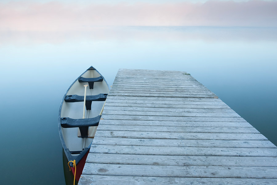 A dock with a canoe alongside, on a misty Lake Audy at Riding Mountain National Park, Manitoba, Canada. Photo by istockphoto.com.