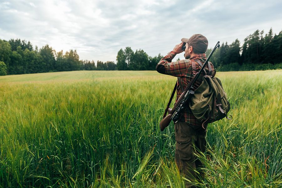A hunter eyeing up his next target, with a rustic backpack and rifle on his back.