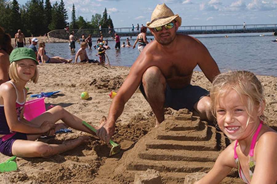A family building a sand castle on the main beach in the townsite of Wasagaming.